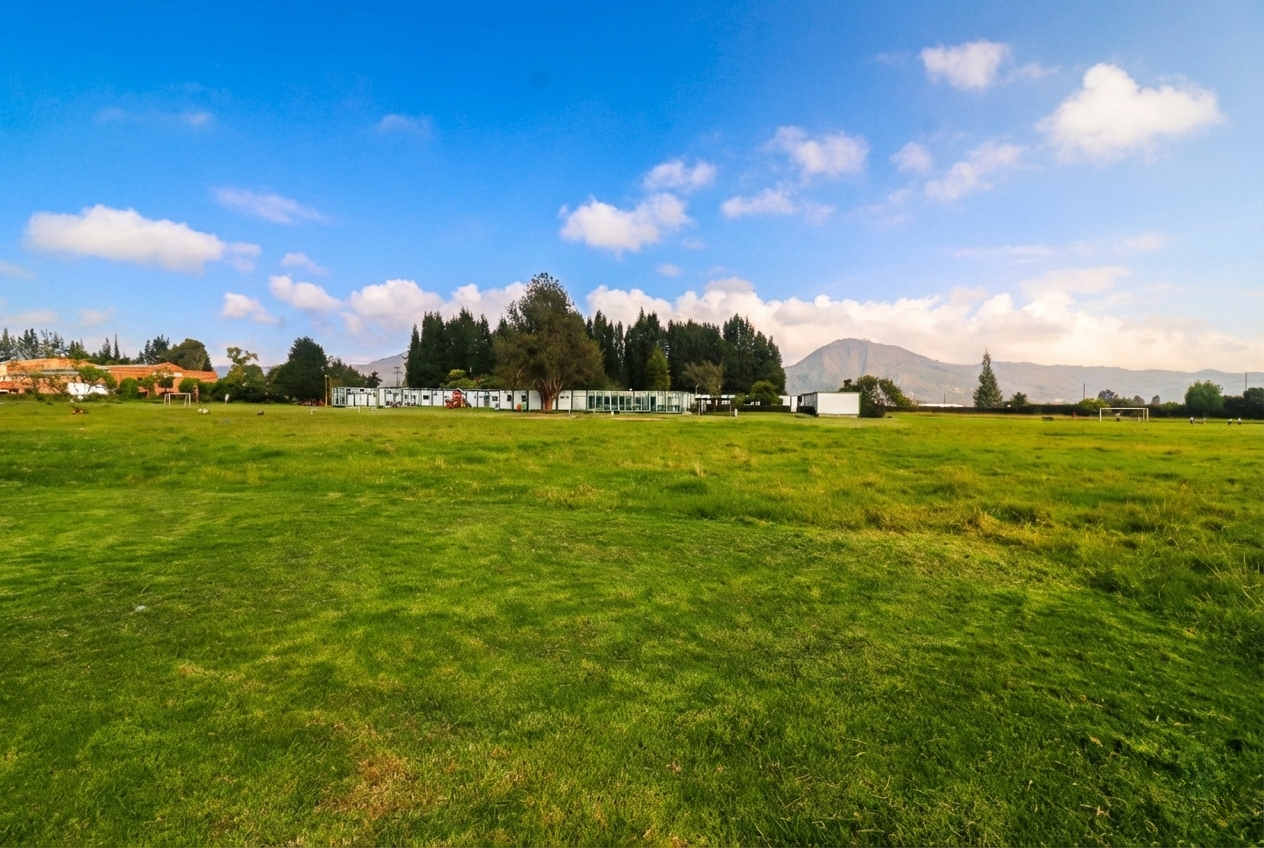 Imagen del campus del colegio, la zona verde en su amplitud y los salones de fondo con la línea de árboles; al fondo, el cerro Majuy de cota.